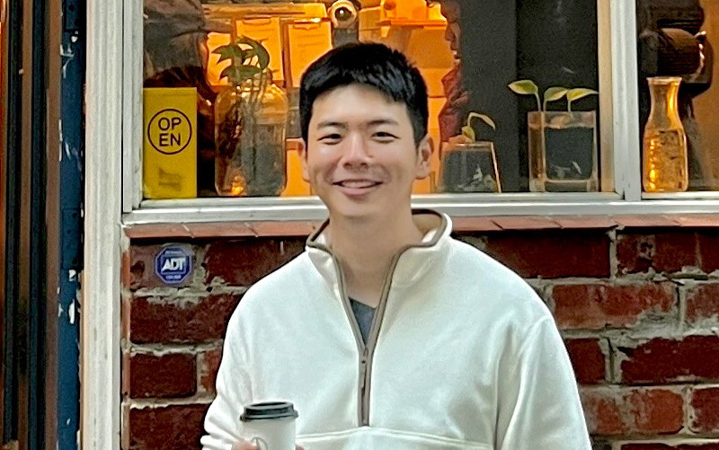 Nelson Niu wearing a white sweater and smiling at the camera against a shop's window.
