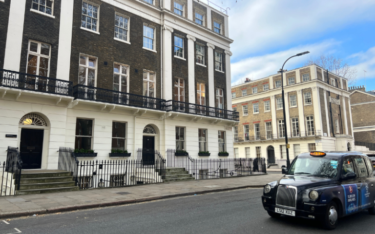 A black cab drives past the department. It is a typical Georgian period London terrace building.