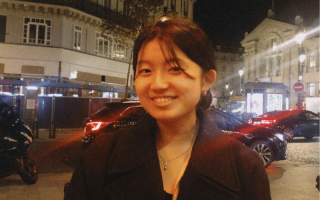 Erika stands in a European street at night. Lights from cars can be seen behind her.