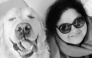 Sarabajaya wears glasses and smiles into the camera with a dog by her side