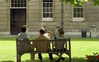Photo of three people relaxing on a bench in the quad