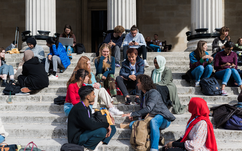 Groups of UCL students sit on the steps of the UCL Portico building.