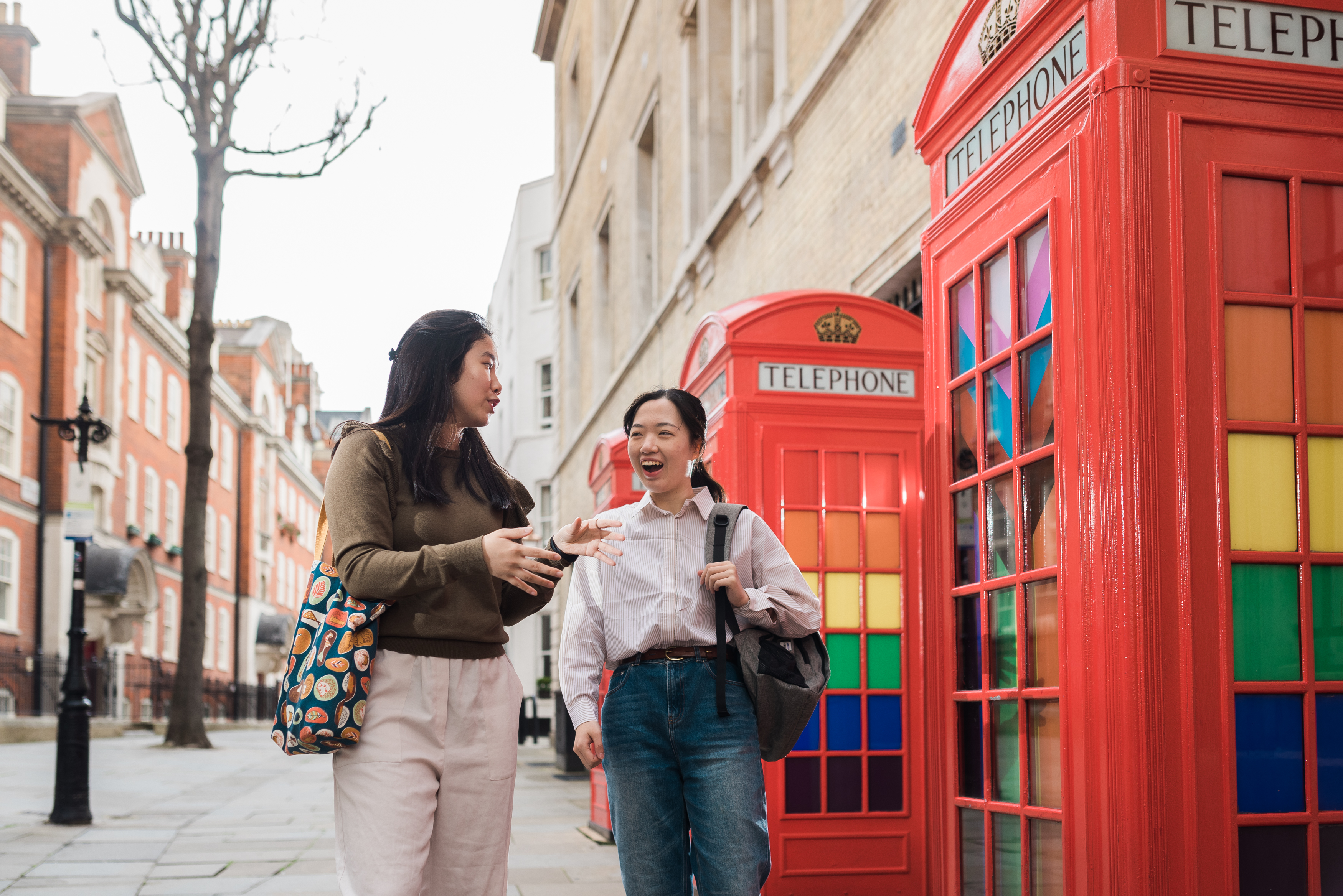 Two students talk and laugh next to two red London telephone boxes.