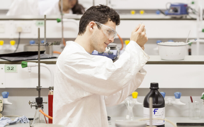 Student in white lab coat works with pipet and beaker. 