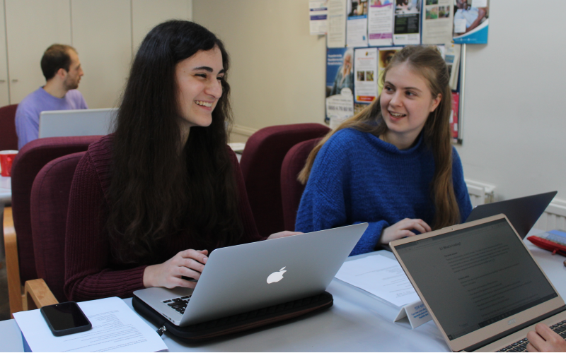 UCL student volunteers work in a school on laptops.