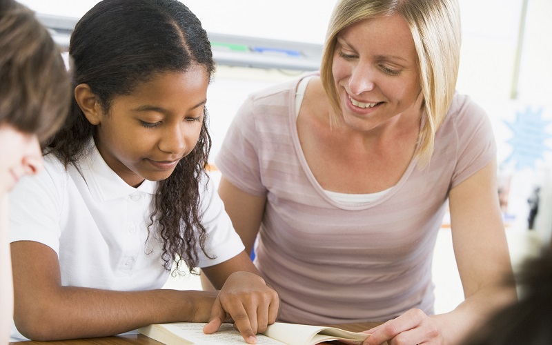 Female teacher and a girl reading a book together, copyright Imagefile