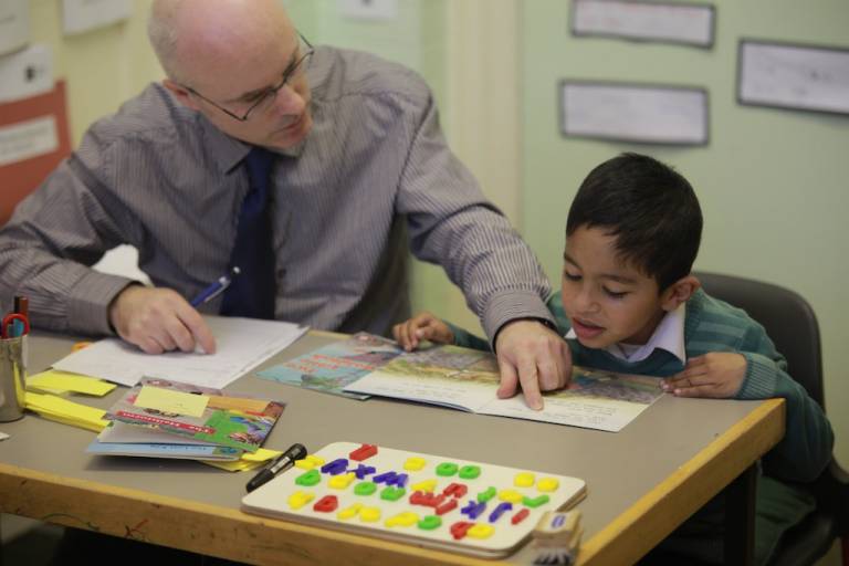 Child reading a book and the Reading Recovery teacher is pointing out a difficult word 