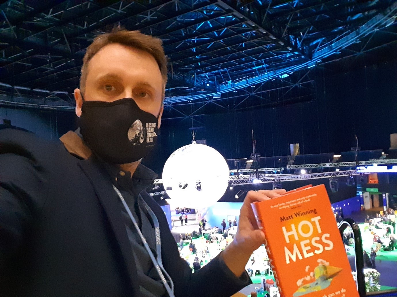 Matt Winning in front of the globe display at COP26 holding his recent book 'Hot Mess'