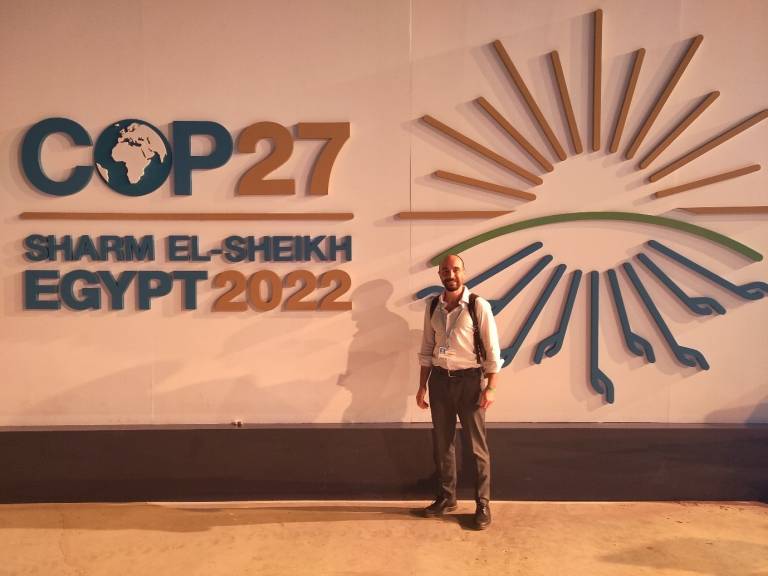 Andrea stands in front of a white lit sign that says COP27 it is dark outside