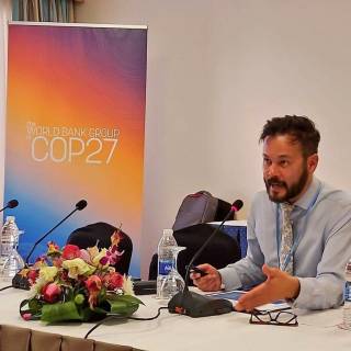 simon sits on a panel infront of a COP27 sign