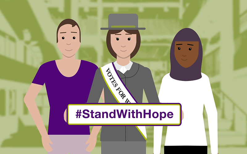 a cartoon image of a lego suffragette holding a sign saying #StandWithHope. A man and a woman stand behind her in the UCL student centre. 