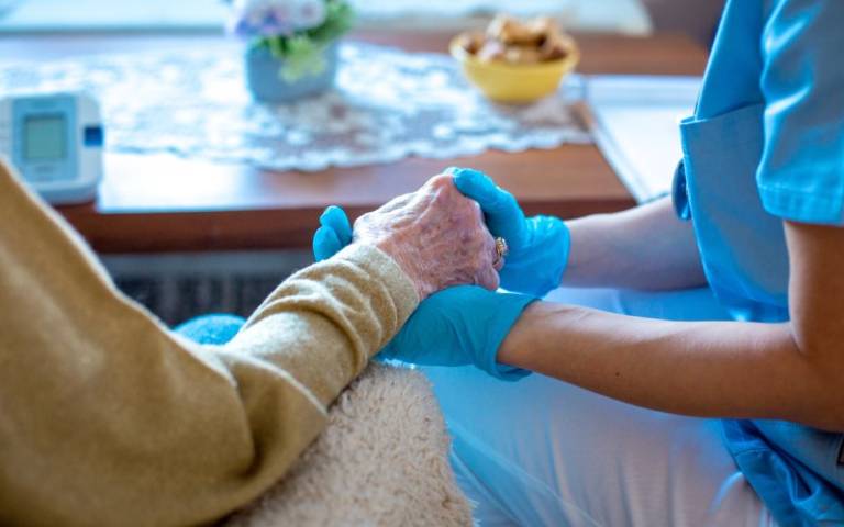 Care worker hold an elderly person's hand while wearing surgical gloves
