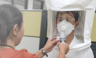 A person wearing a facepiece with a testing hood over the top and a bitter or sweet spray is being sprayed into the hood by the face fit tester