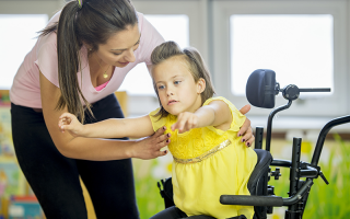 A caregiver is helping a little girl out of her wheelchair
