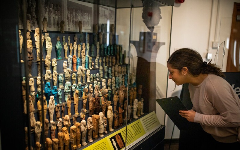 Student looking into museum cabinet containing Egyptian shabtis