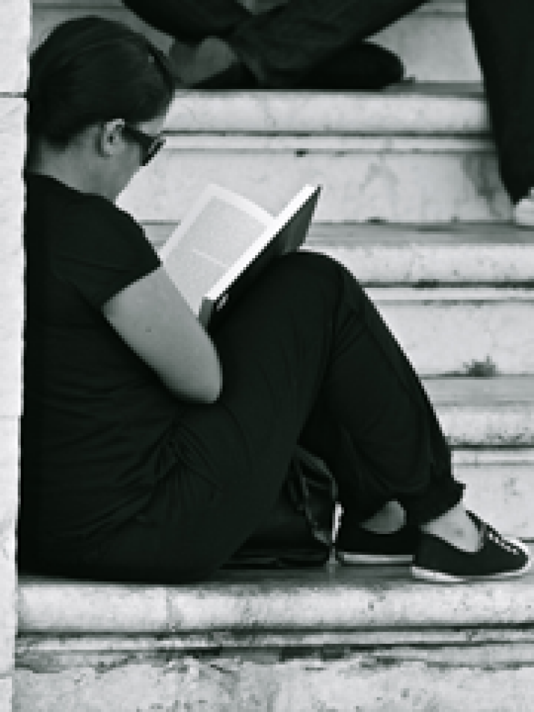 Woman sitting on step reading book…