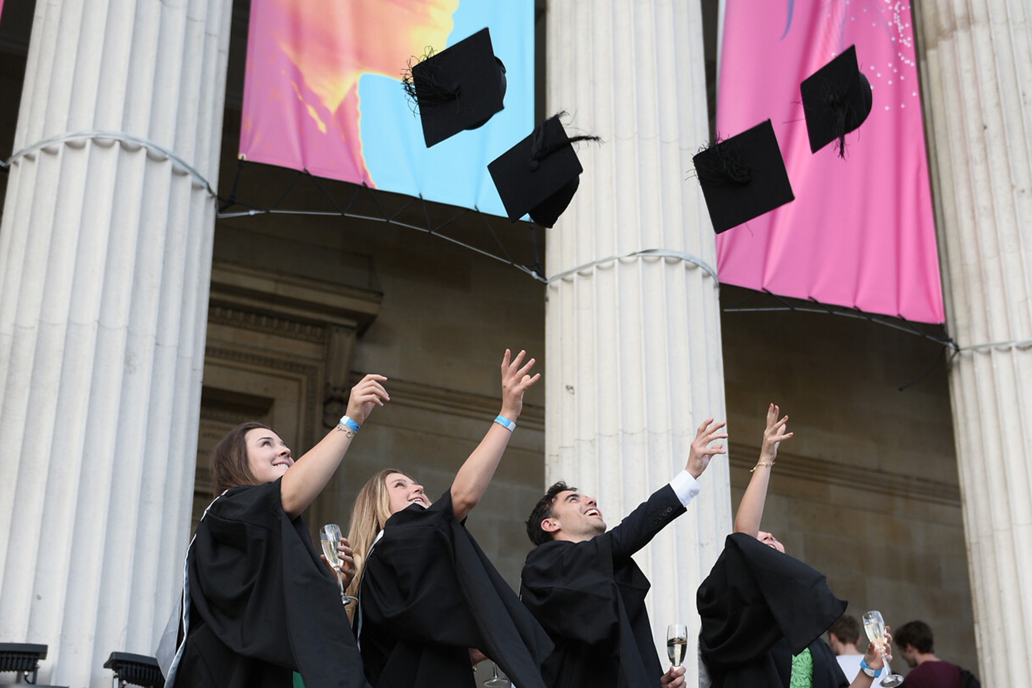 Four students dressing in graduation gowns, throwing their graduation caps