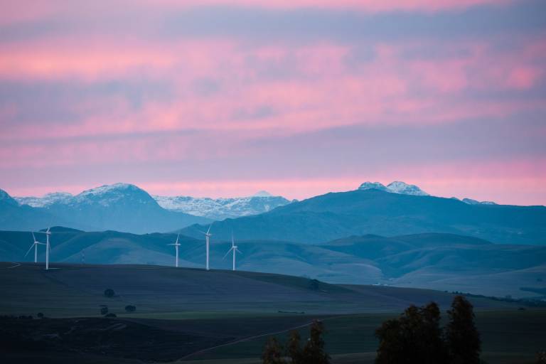 Wind turbines with snowcapped mountains in the background during sunset
