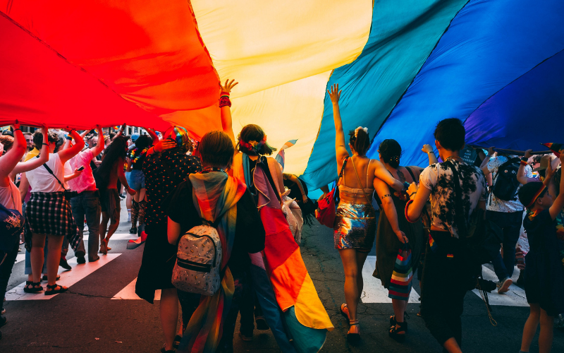 a group of people stand under a rainbow flag
