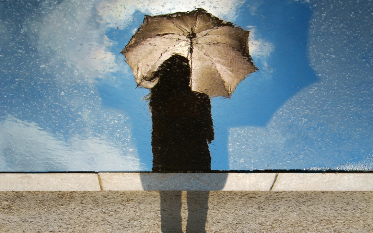 Reflection of girl with umbrella in puddle 