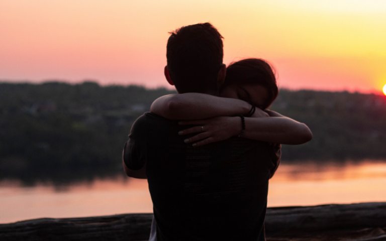 Two people hugging with a sunset in the background