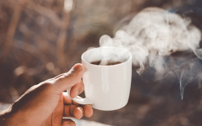 A hand holding a steaming mug of coffee
