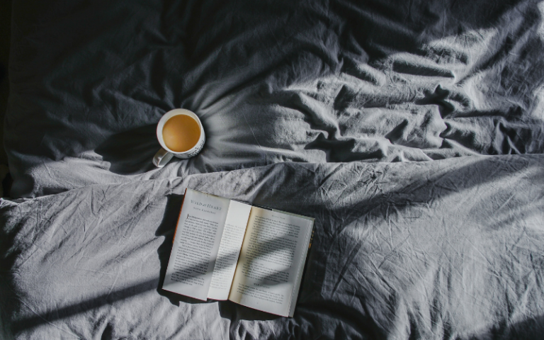 View of a bed, with a cup of team and notebook