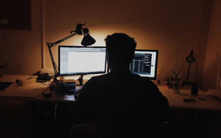 Man in dark illuminated by two computer screens in a dark room