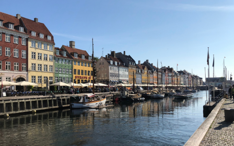 View of Copenhagen riverfront, with tall houses in the background and boats floating on the river