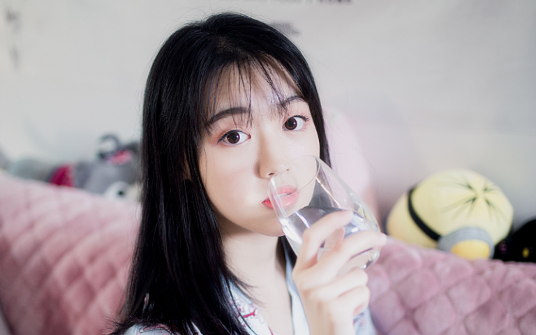 Asian student sitting on a pink couch drinking a glass of water