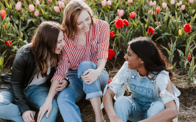 three female friends sitting in field of tulips