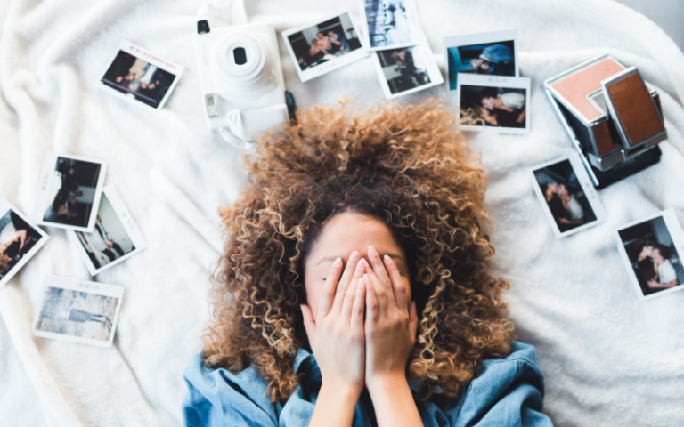 Girl lying on bed surrounded by polaroids