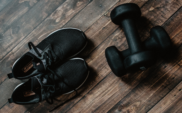 black pair of trainers and dumbells on laminate flooring