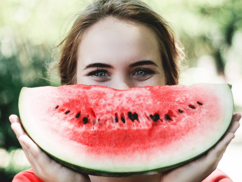 Woman holding a slice of watermelon in the shape of a smile