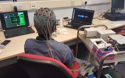 A person wearing an encephalogram headset, wired to a monitor, with instructions on a laptop
