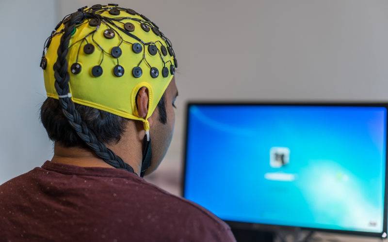 Person wearing a cap as an electroencephalogram in front of a screen with an MS Windows display
