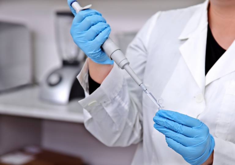 Photograph of the hands of someone working in a lab wearing blue gloves.