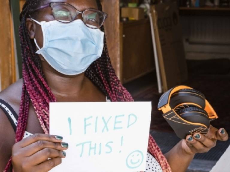 Woman holding up headphones alongside a sign that reads: 'I fixed this'.