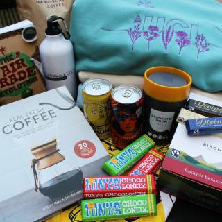Image of hamper goodies including: jumper, drinks, mug, reusable bottle. chocolate bars, coffee