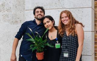 3 students smiling holding a plant