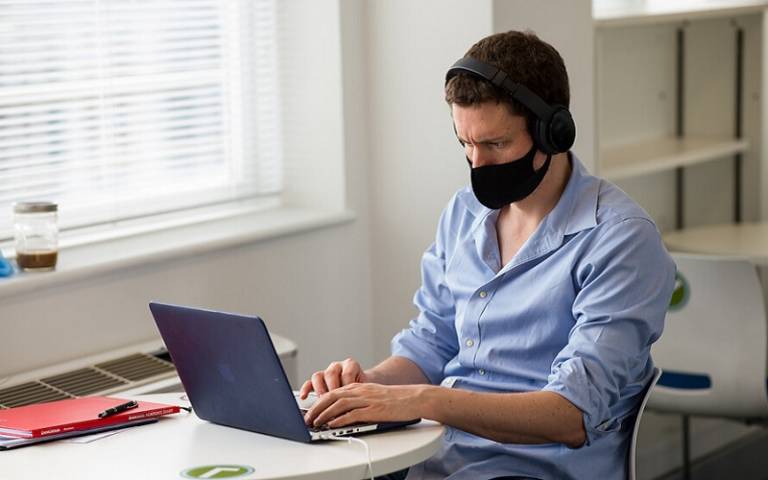 Man with mask and headphones typing on laptop