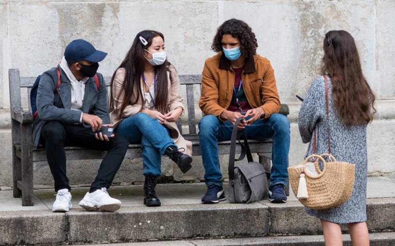Students in masks gathered chatting on a bench