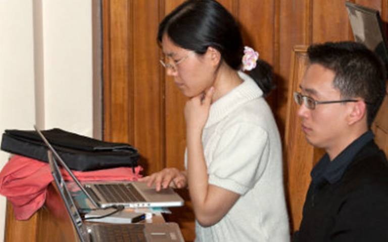 Two students looking at laptops during a lecture in a lecture hall