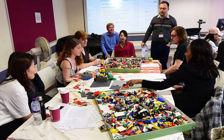 A classroom with students sitting in groups playing with big trays of lego