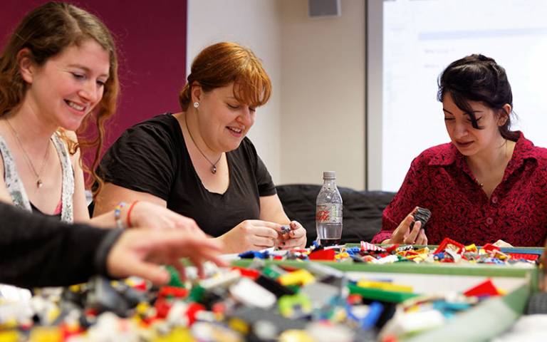 three students playing with lego and smiling