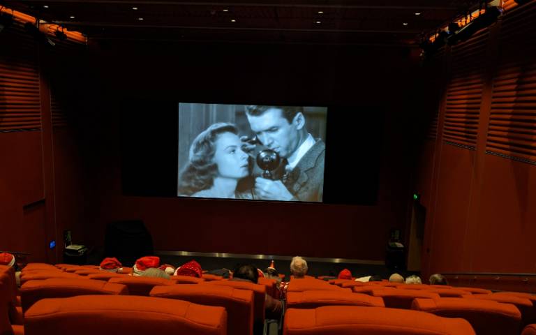 A screen showing a black and white film in a cinema seen from behind the audience