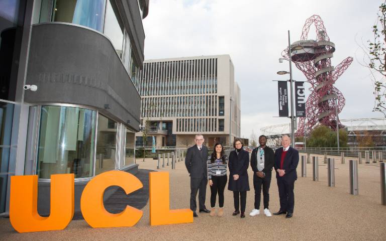 UCL staff and students outside One Pool Street next to giant orange U-C-L letters with Marshgate and the ArcelorMittal Orbit and London Stadium in the background