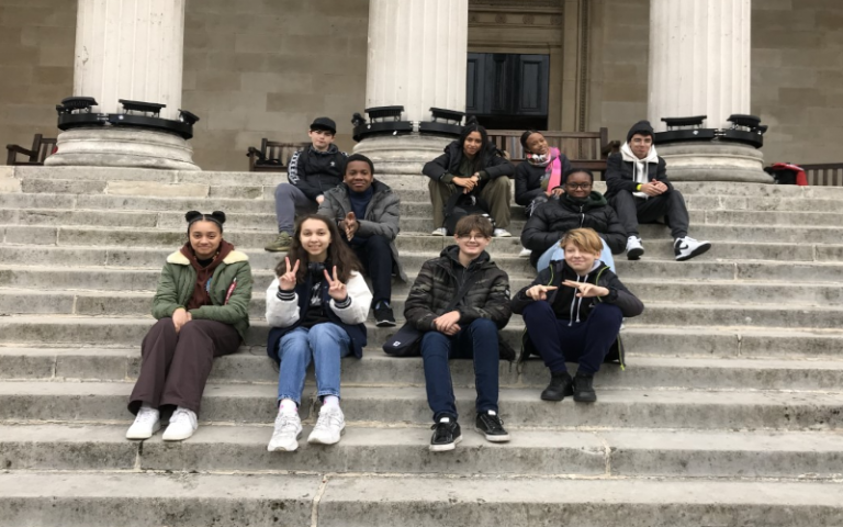 A group of young teenagers sit on the steps of the Portico at UCL