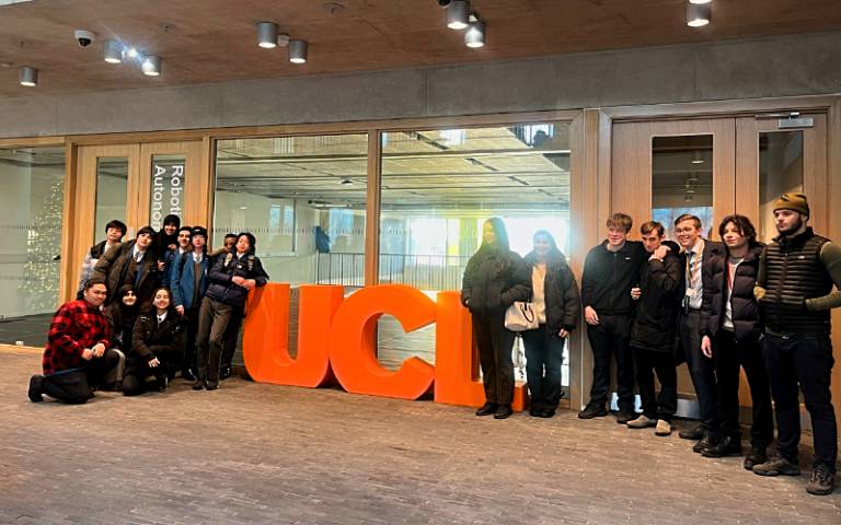 A group of schoolchildren assembled either side of large orange letters spelling out U-C-L in the ground floor reception of One Pool Street on the UCL East campus