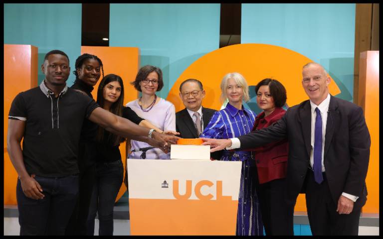 A group of people gathered around a UCL branded lectern with a giant button on it, sharing the pushing of the button